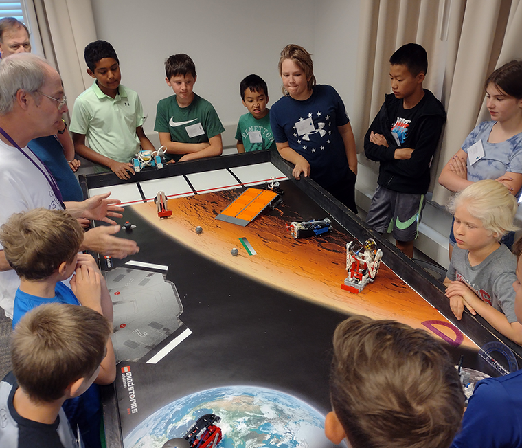 Introduction to Robotics Campers clustered around the mission board, discussing strategy with the staff.