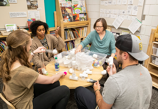 Link, Educators experiencing STEM activities within the RCEDE's model early learning classroom.  Walls are decorated with examples of student work, materials are close at hand.